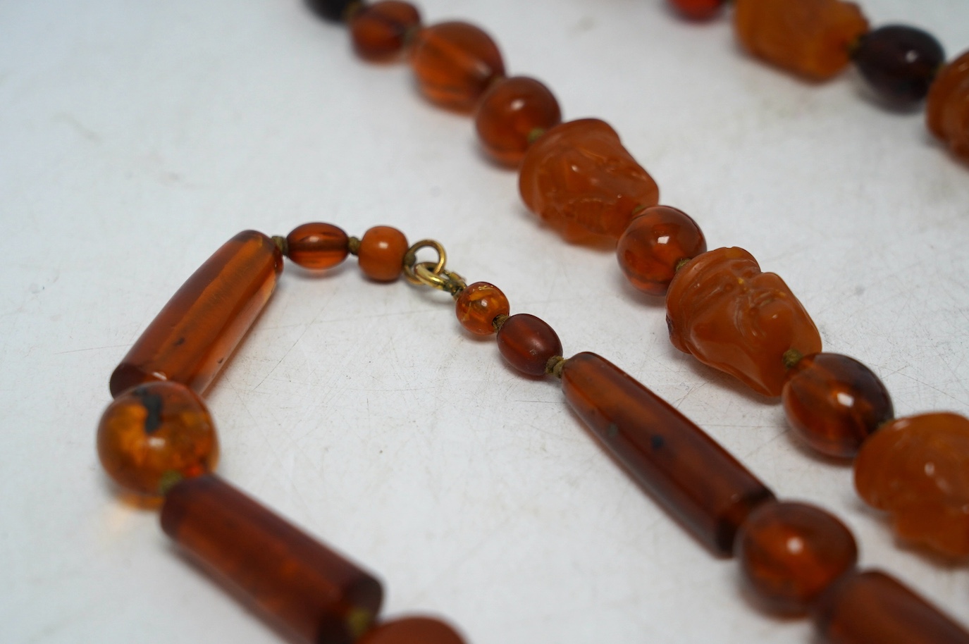 Two amber bead necklaces including Chinese with carved busts, 76cm and a pair of drop earrings, gross weight 145 grams. Condition - poor to fair
